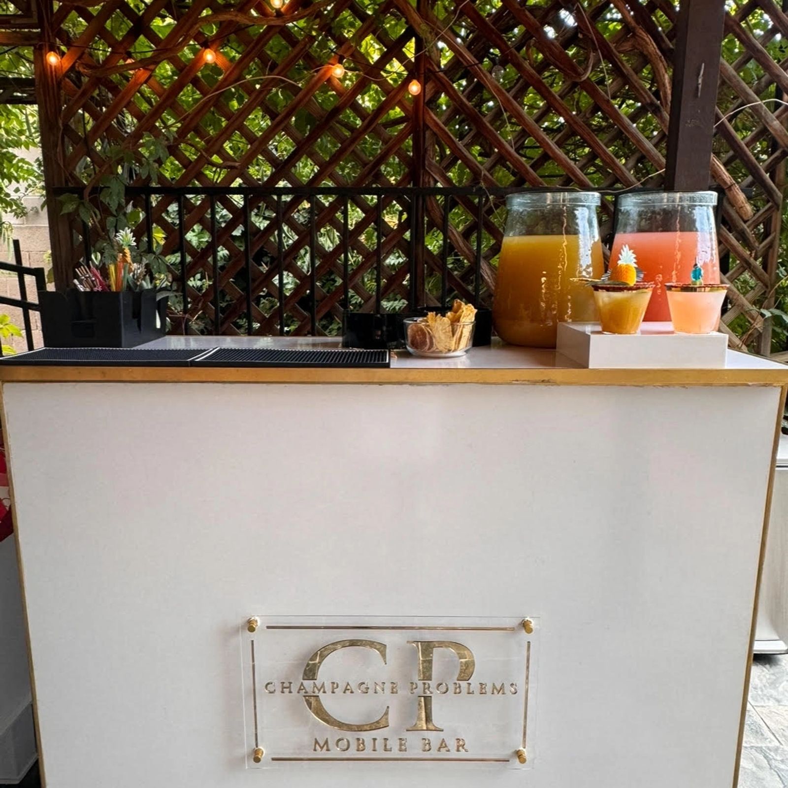 Mobile bar set up on a string-lit patio with juice dispensers and garnishes